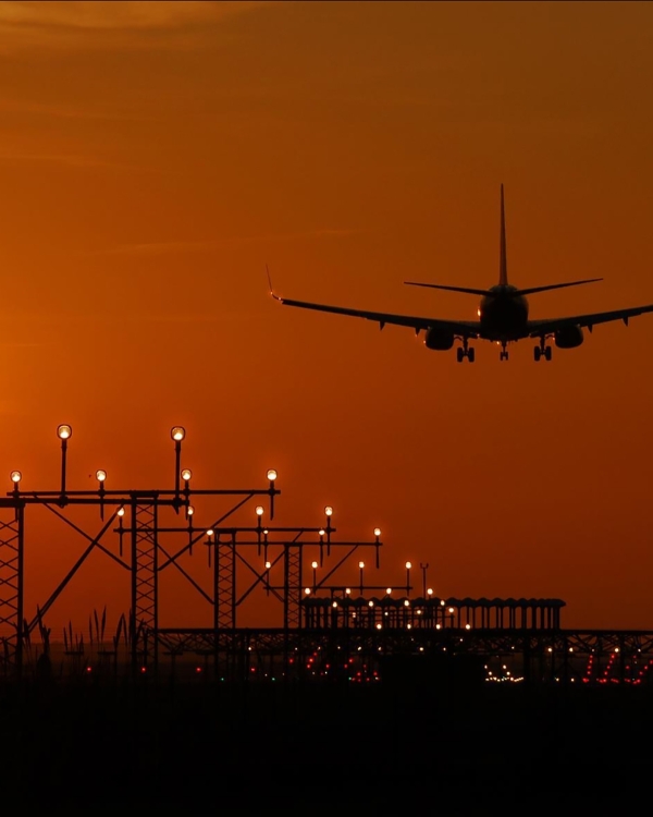 Silhouette of an airplane landing during sunset at Barcelona airport, with a vibrant orange sky.