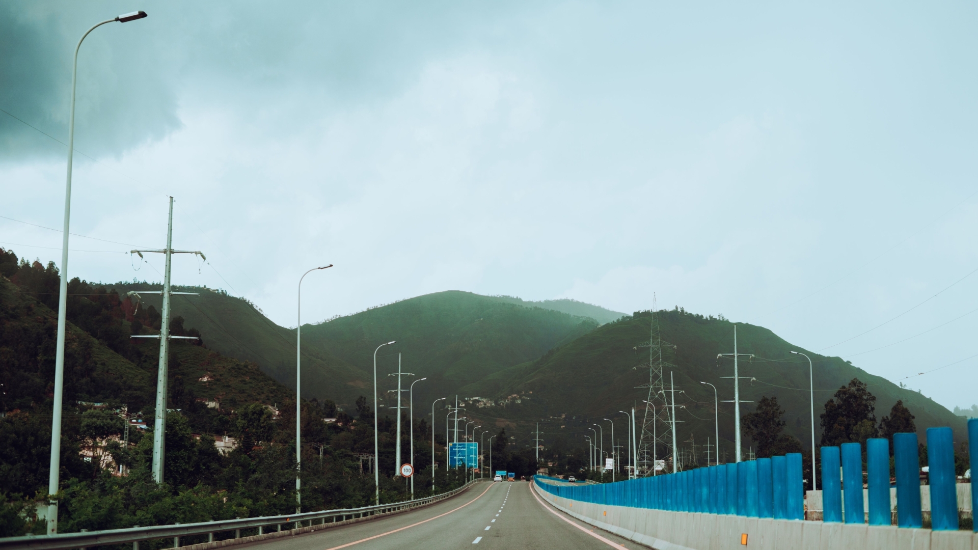 A quiet highway stretches towards green mountains under an overcast sky, ideal for stock photography.