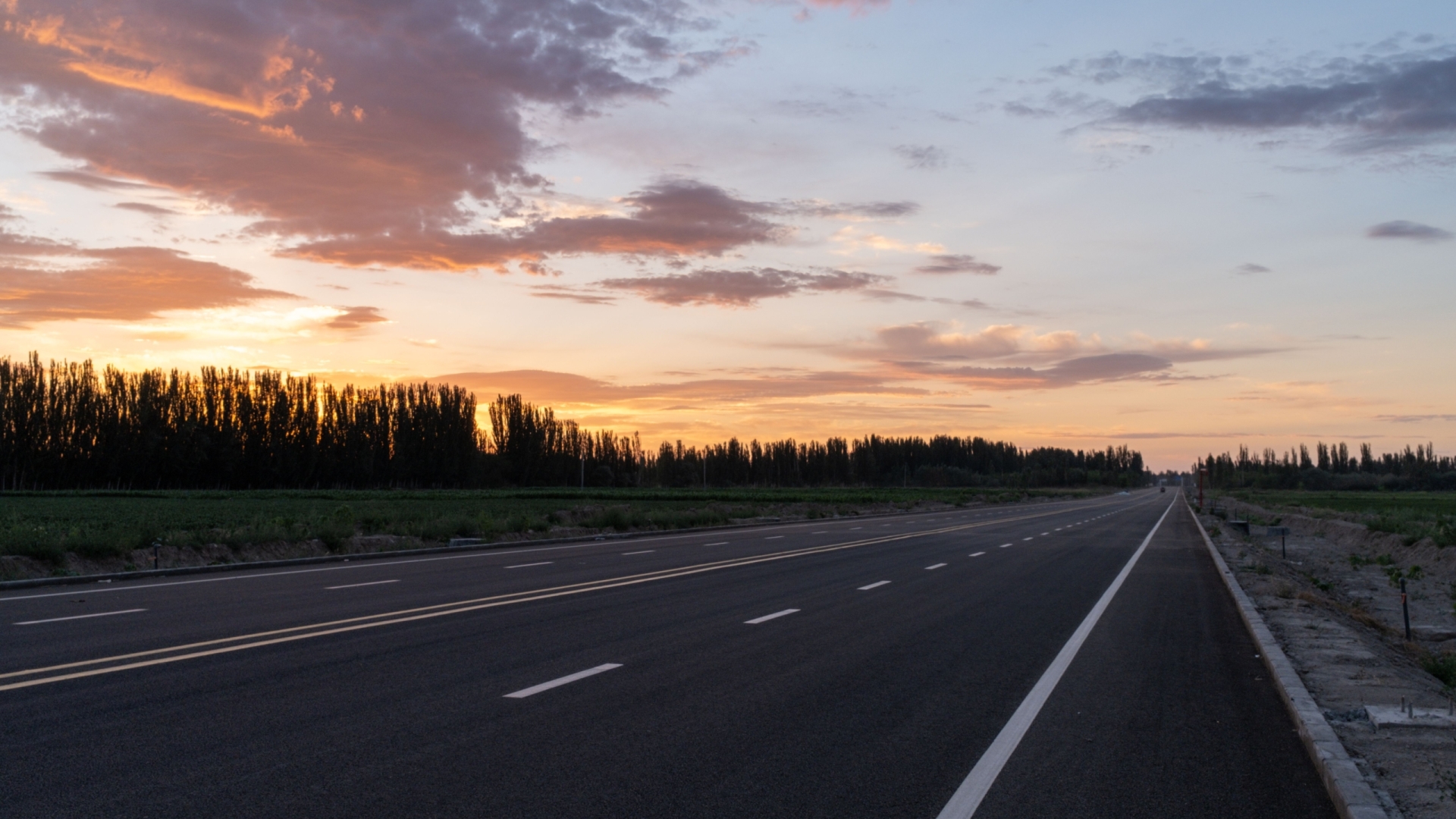 A peaceful highway stretching into the horizon under a colorful sunset sky.