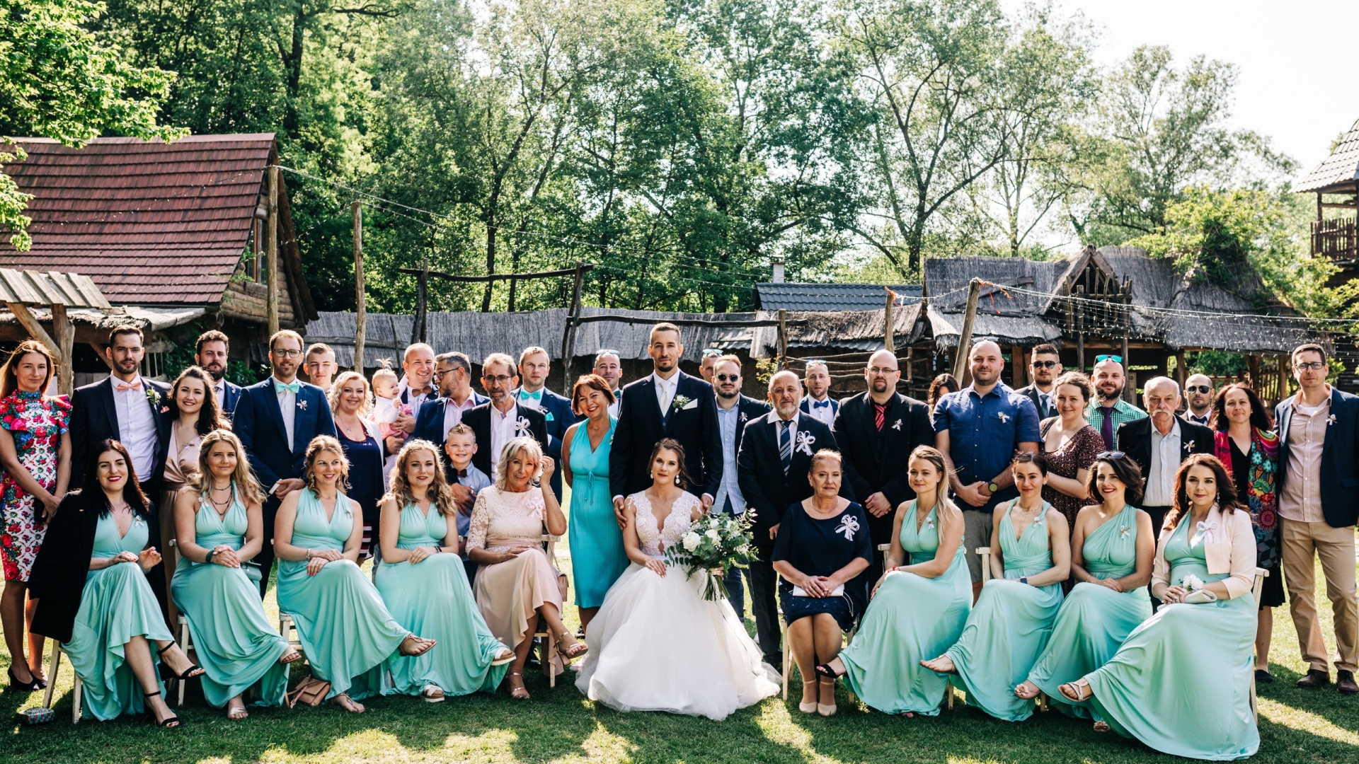 Large group photo of wedding guests outdoors on a sunny day.