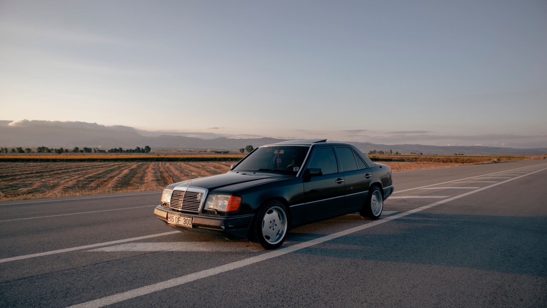 A vintage black car parked on an empty rural road at sunset, capturing serene countryside vibes.