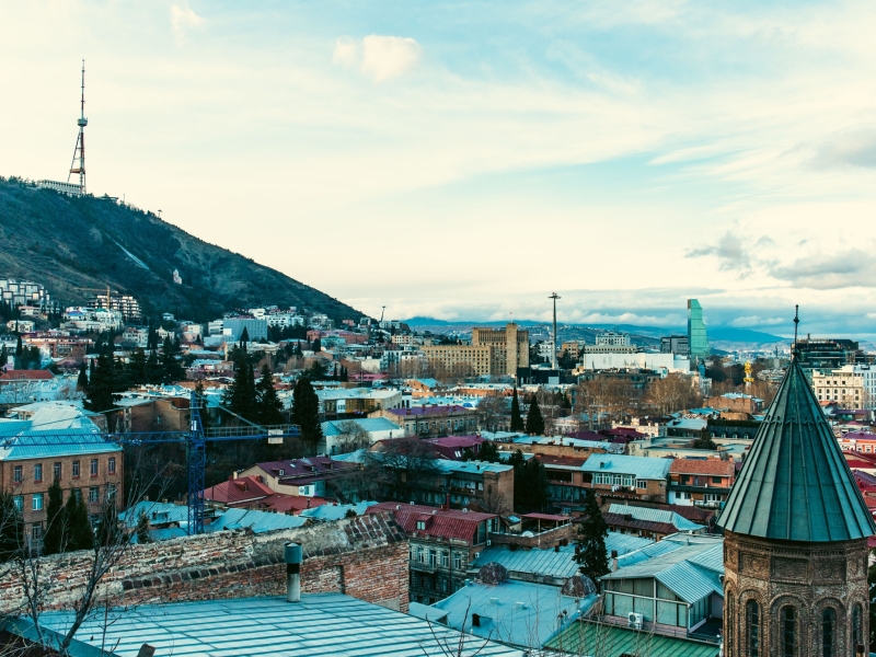 Aerial view of Tbilisi showcasing iconic landmarks and vibrant cityscape under a clear sky.