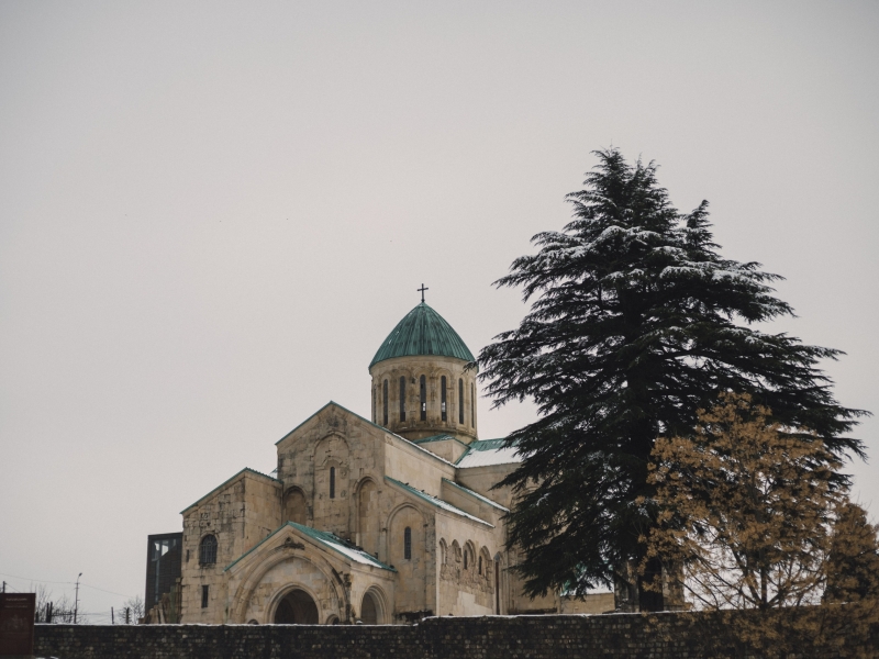 A serene winter view of a historic cathedral in Tbilisi, Georgia with snow-covered trees.