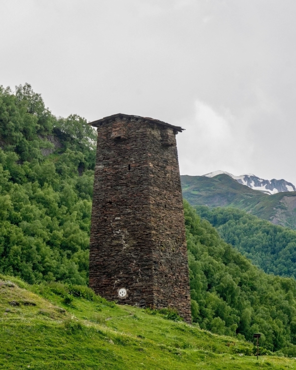 Stone tower in Mestia, Georgia amidst lush green hills and mountains.
