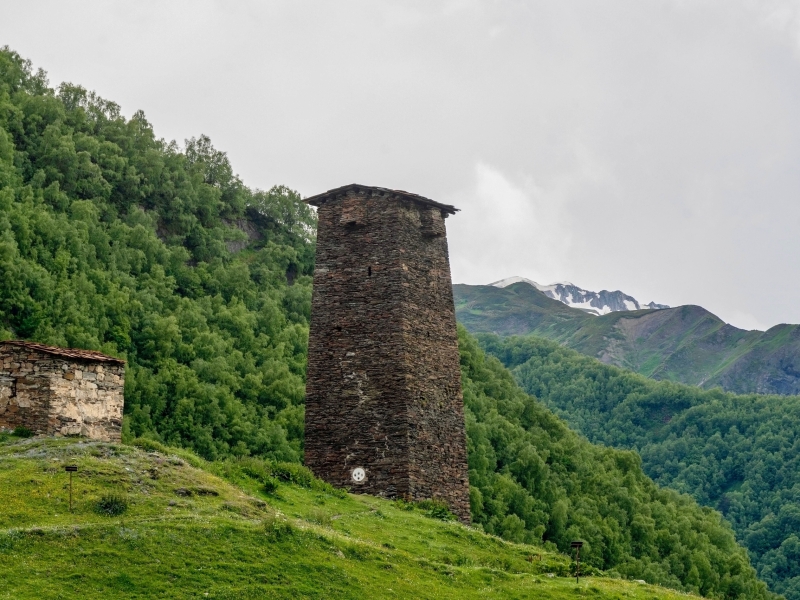 Stone tower in Mestia, Georgia amidst lush green hills and mountains.