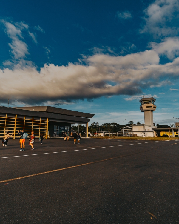A small airport terminal with people walking on the tarmac under a blue sky.
