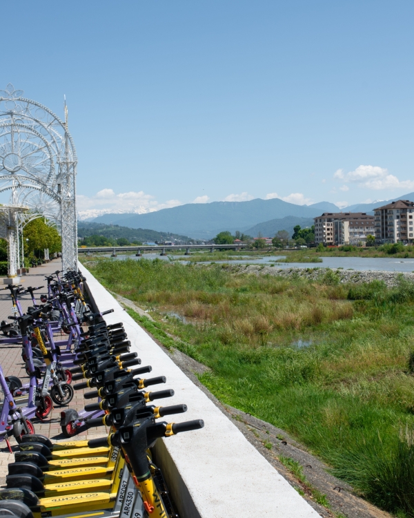 Electric scooters lined up on a riverside walkway under a clear spring sky.