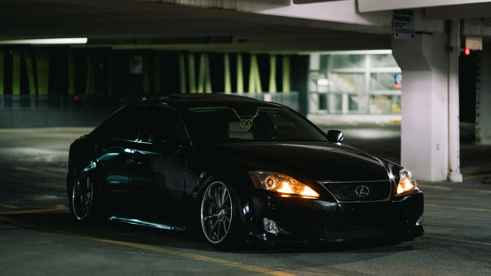 Elegantly parked black Lexus sedan under dim garage lights, exuding luxury and sophistication at night.