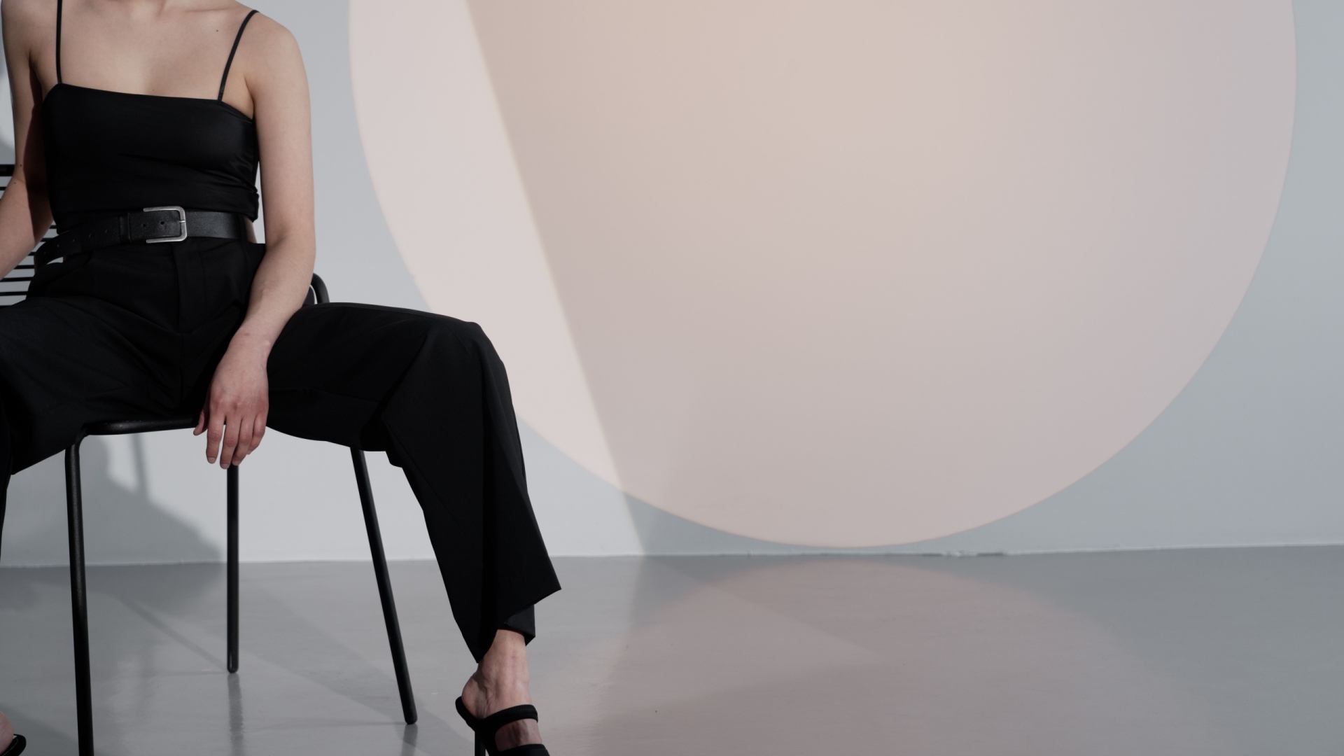 Elegant woman in black outfit posing in stylish studio with minimalist design.